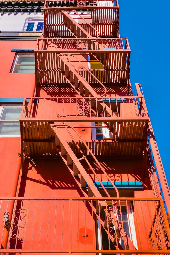 Low-angle view of a vibrant red building with a distinct fire escape staircase against a clear blue sky.