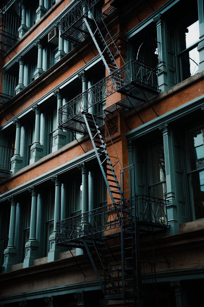 Close-up of a vintage brick building facade with prominent fire escapes and green window frames.