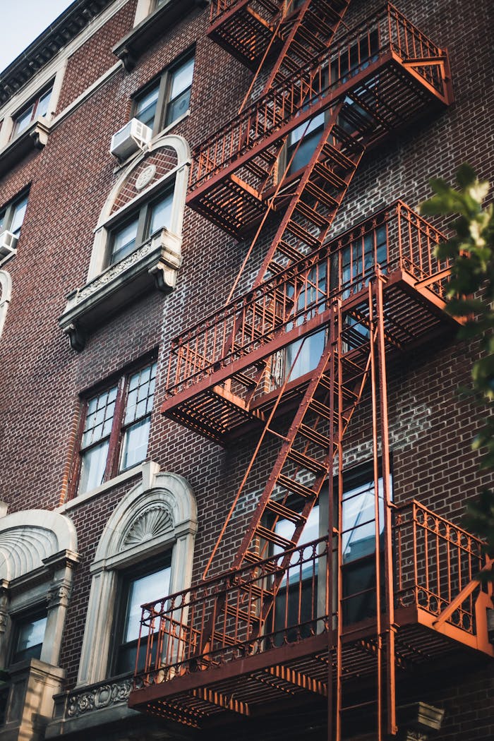 Low angle shot of a brick building featuring metal fire escape stairs and glass windows.